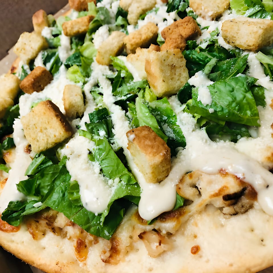 Close-up of a Bada Bing Pizzeria Caesar salad pizza with chicken, lettuce, croutons, and dressing.