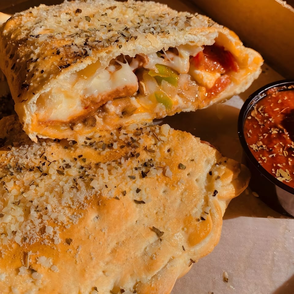 A Bada Bing Pizzeria calzone, sliced open to reveal melted cheese, pepperoni, and green peppers, with a side of marinara sauce.