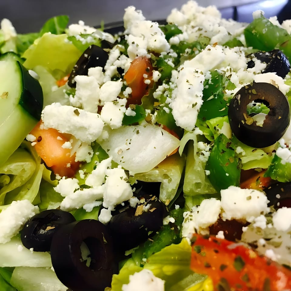 Close-up of a fresh Bada Bing Pizzeria salad with lettuce, cucumbers, tomatoes, olives, and feta cheese.