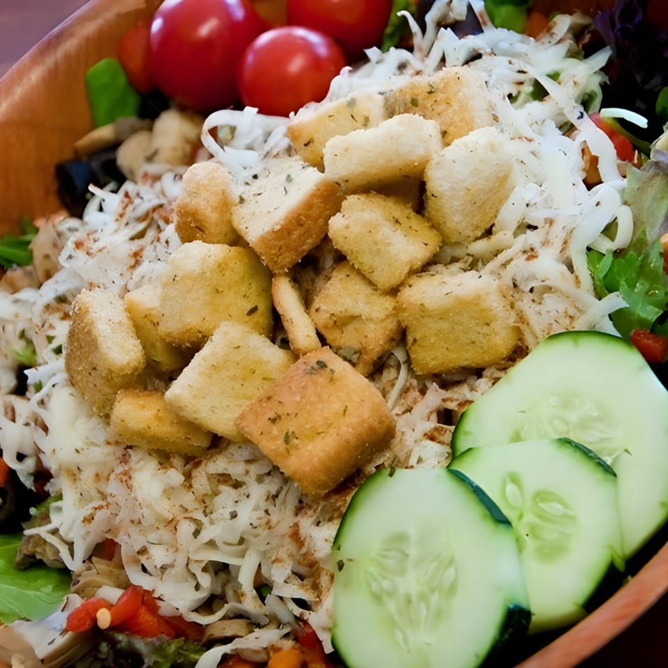 Close-up of a fresh salad with croutons, shredded cheese, cherry tomatoes, and cucumber slices.